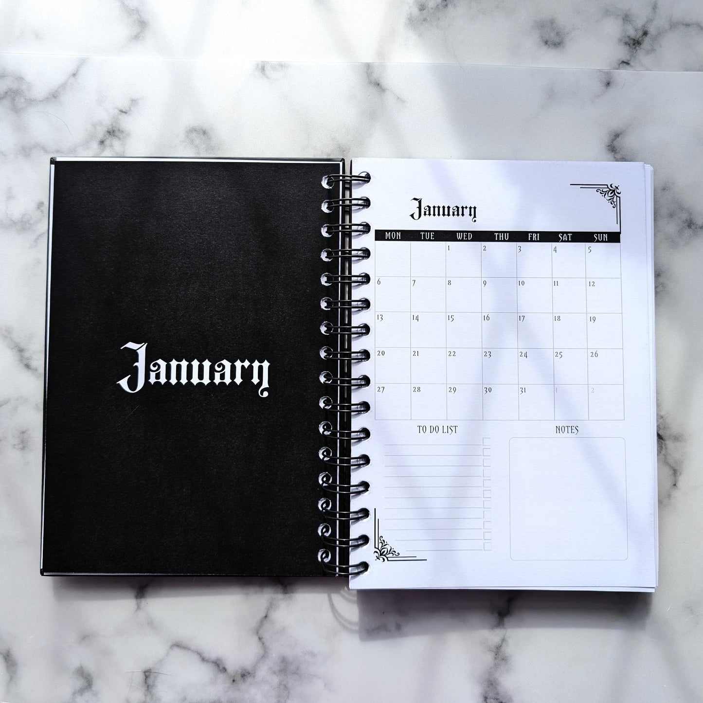 A two page layout inside the 2025 Planner by Gothic Office. The page on the left says January in a gothic font, in white on a fully black page.  The right page is a table of the month January, a To Do List and Notes section. 