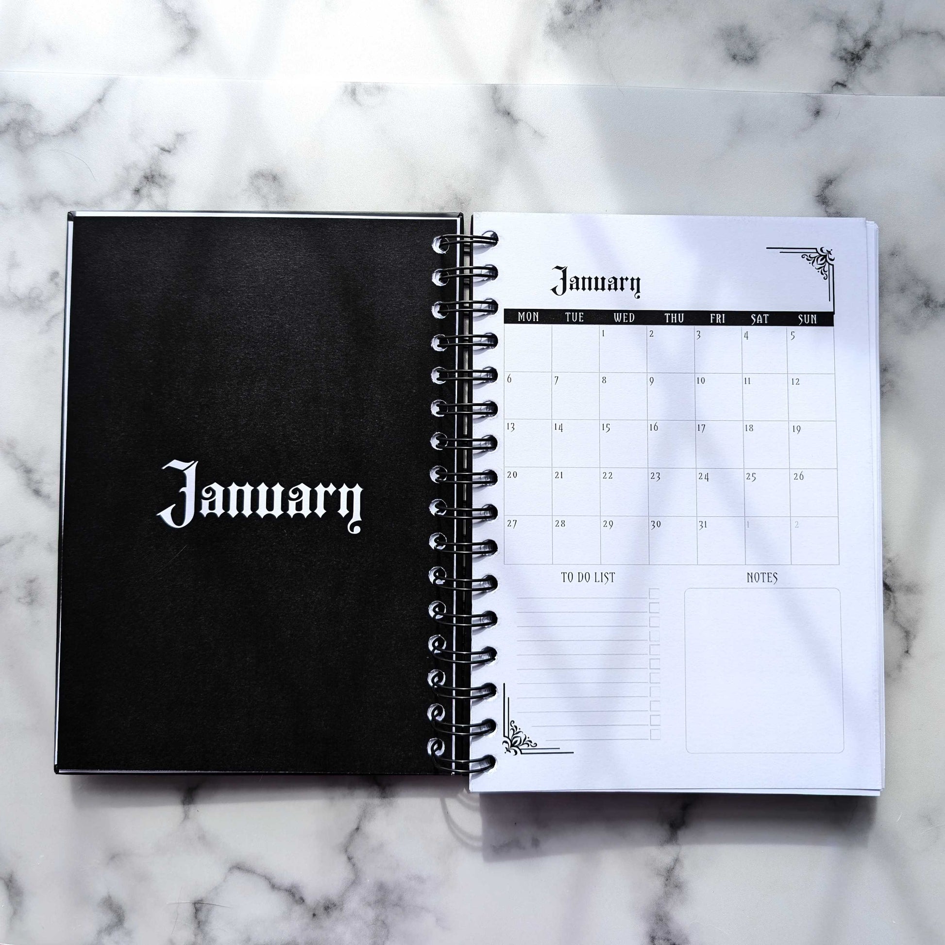 A two page layout inside the 2025 Planner by Gothic Office. The page on the left says January in a gothic font, in white on a fully black page.  The right page is a table of the month January, a To Do List and Notes section. 
