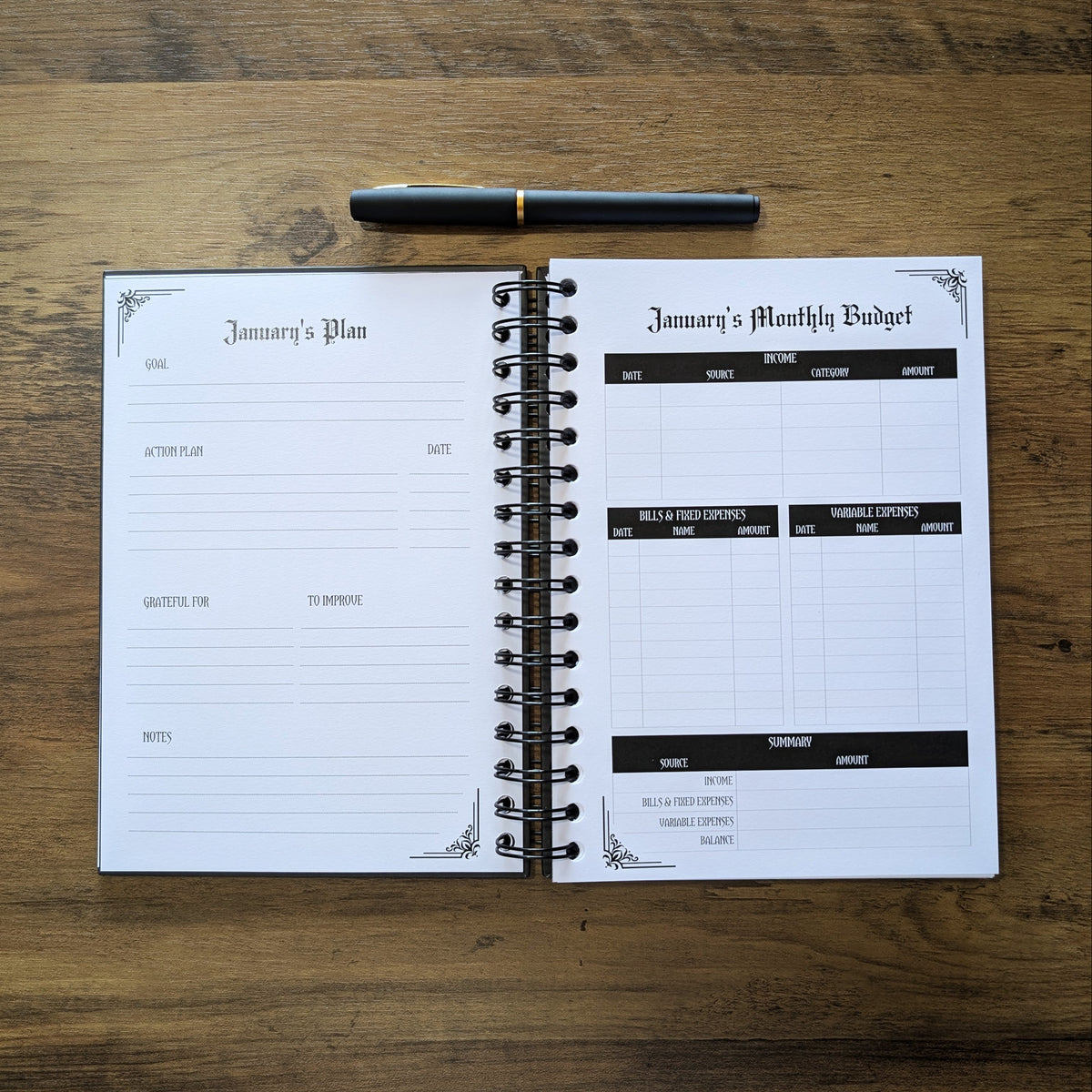 An open spiral-bound planner showing a January plan and monthly budget page, placed on a wooden tabletop with a black pen above it.